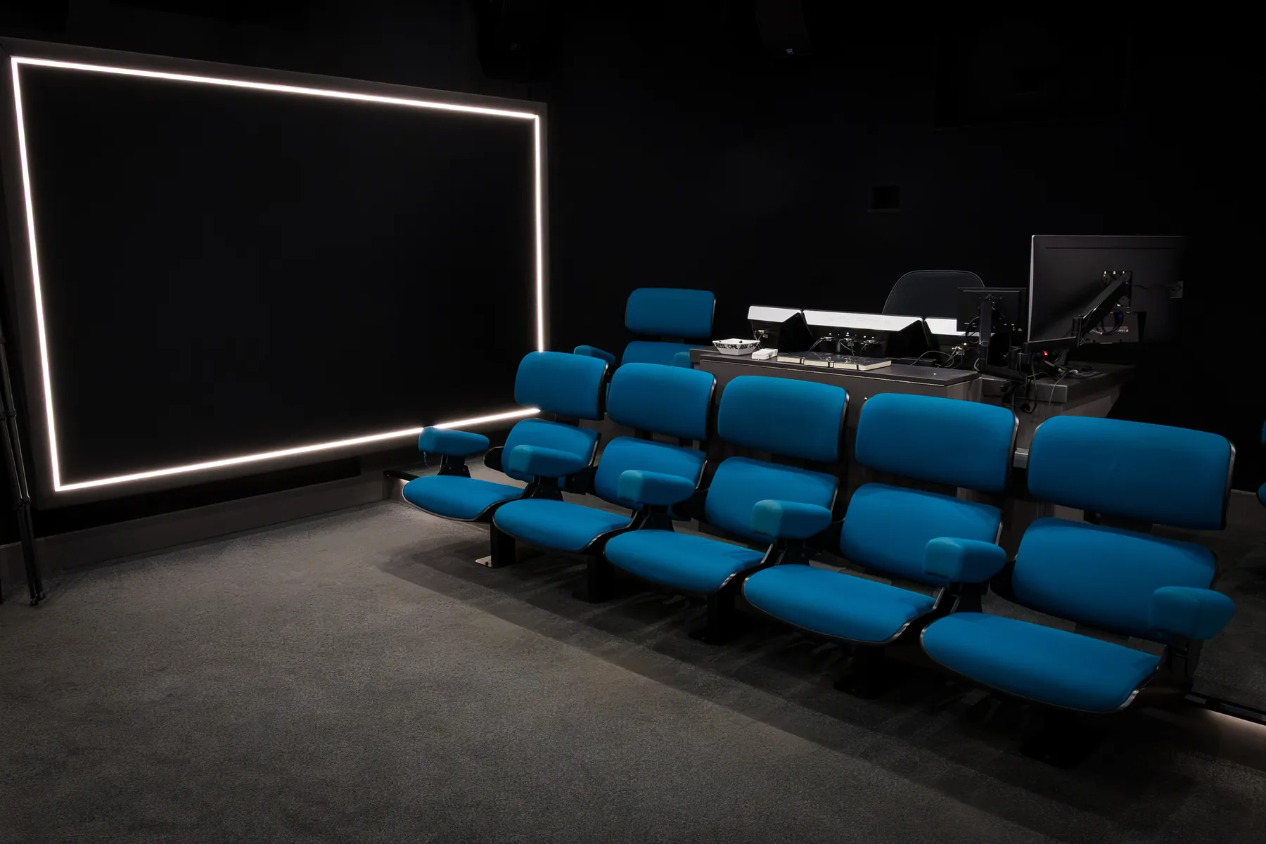 La sala cinema vista dal fondo, con lo schermo illuminato e le poltrone blu